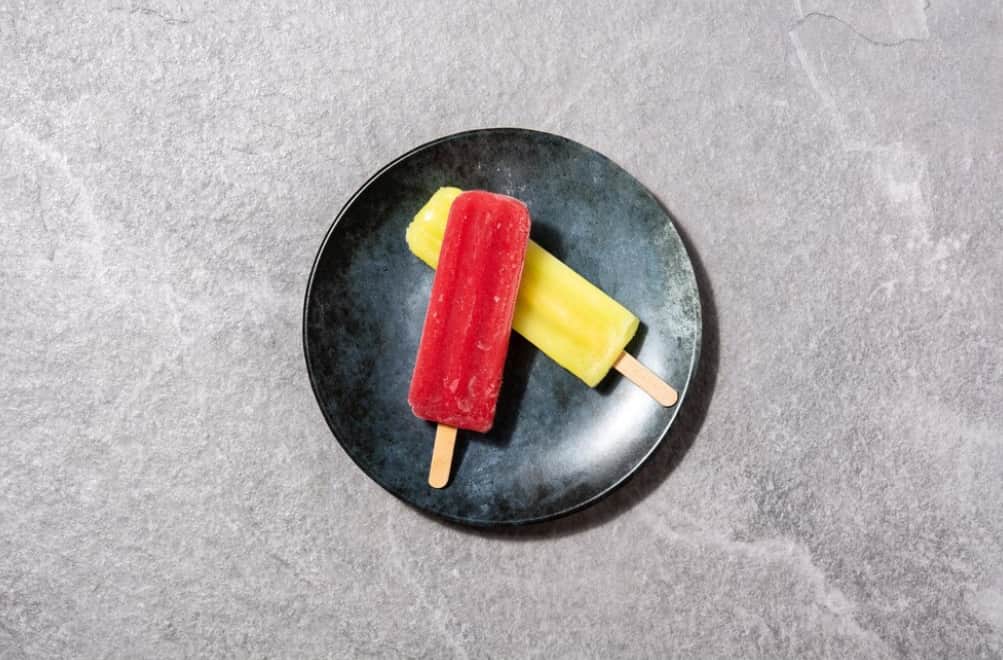Two fruit ice pops on a dark round plate on a gray surface