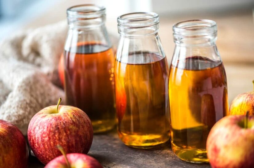 Bottles of apple cider vinegar beside fresh apples on wood