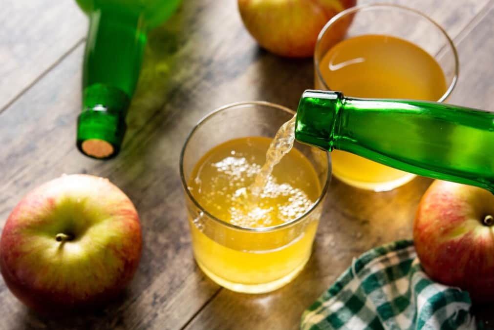 Cider being poured into a glass next to apples on a table