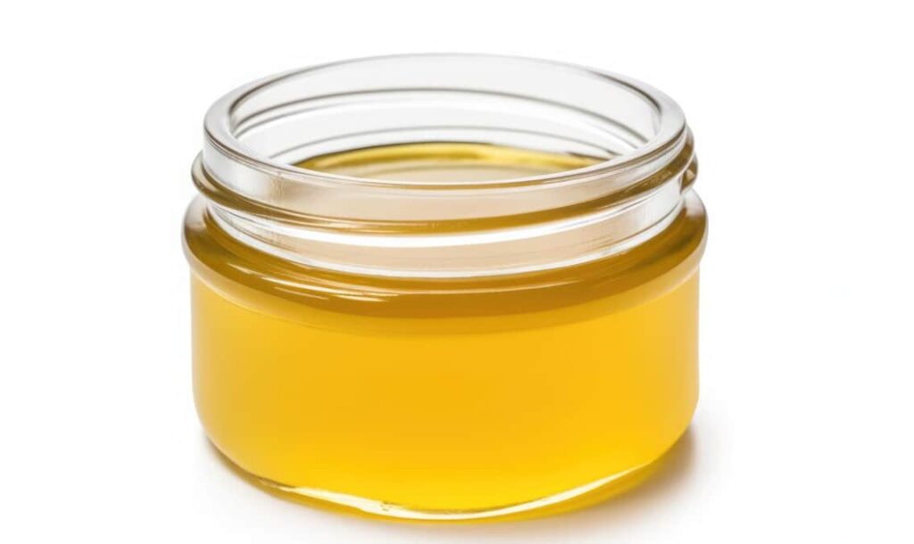Bright yellow ghee in a glass jar against a white backdrop