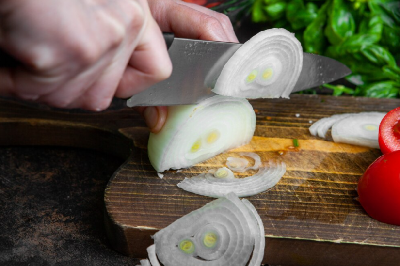 Hand slicing onions on a rustic wooden board