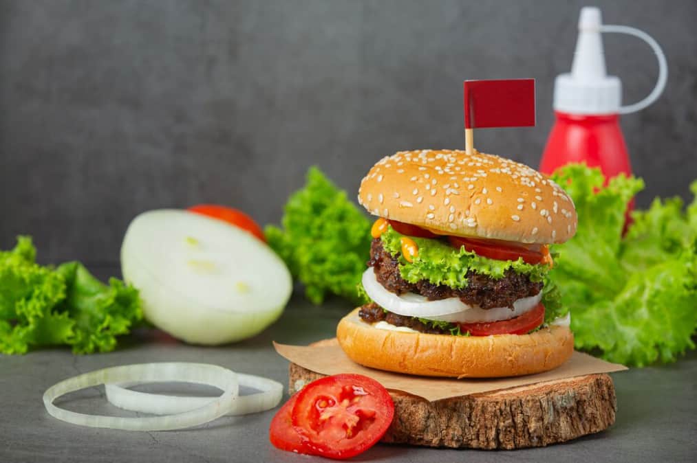 A juicy burger with a red flag on top, next to fresh ingredients