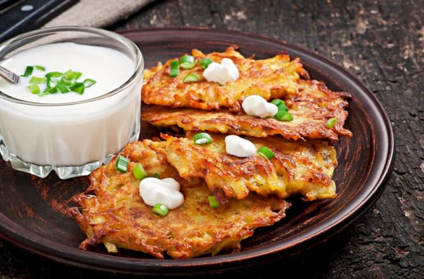 Hash browns with sour cream and green onions on a rustic plate