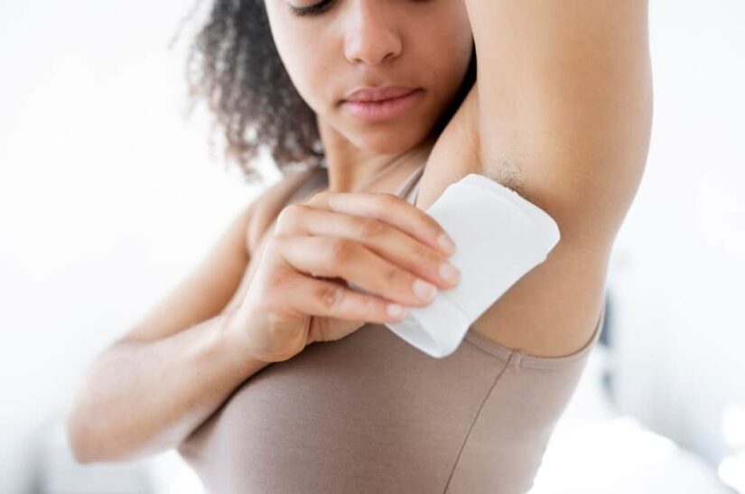 A woman applies roll-on deodorant to her underarm