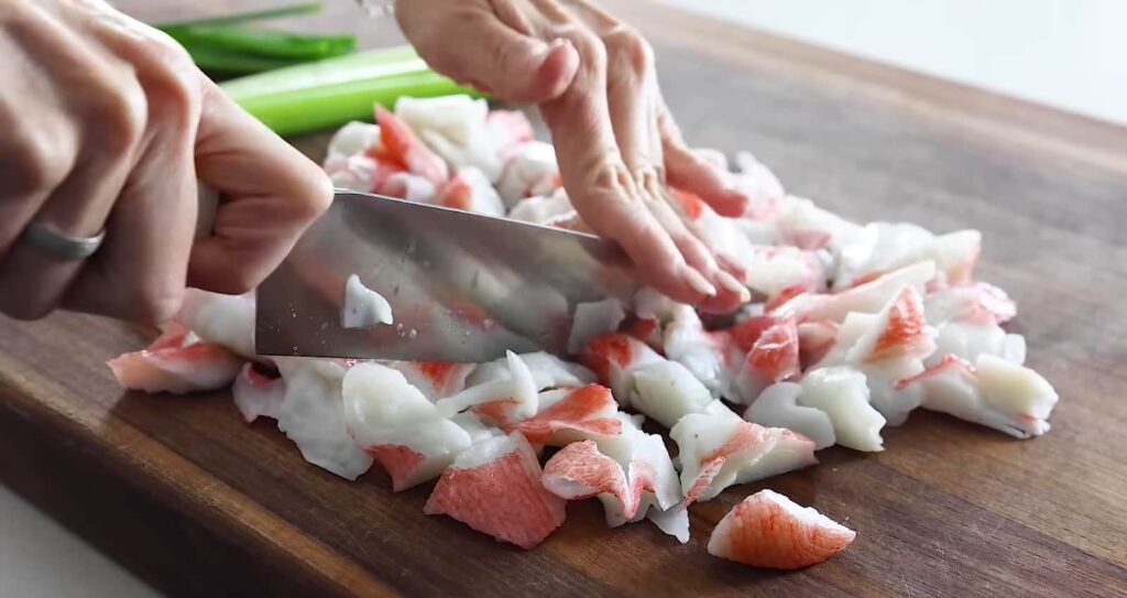 Hands chopping crab meat on a wooden cutting board