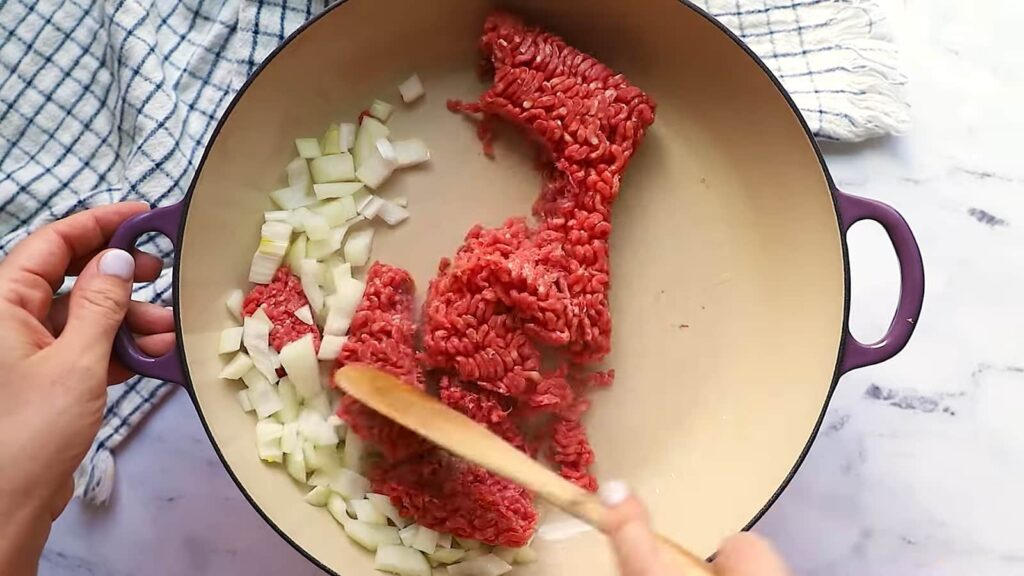 Sautéing diced onions and ground beef in a large purple skillet