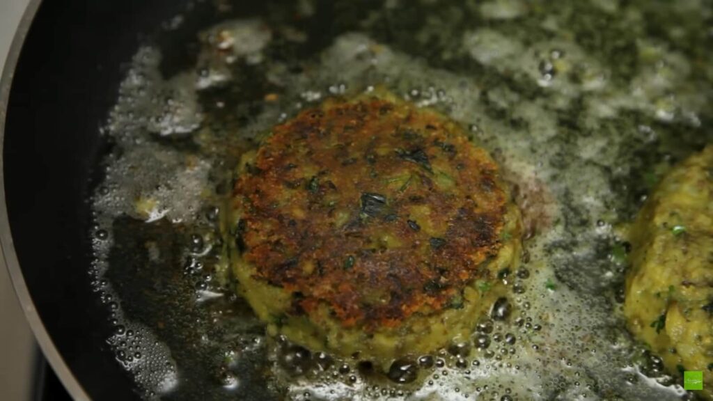A mung bean patty sizzles in a pan with bubbling oil