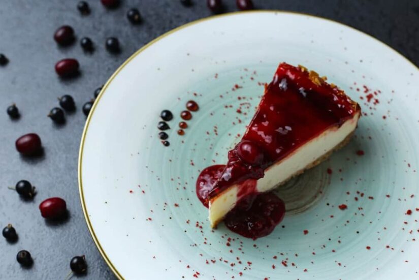 A slice of cheesecake with berry topping on a speckled plate with scattered berries